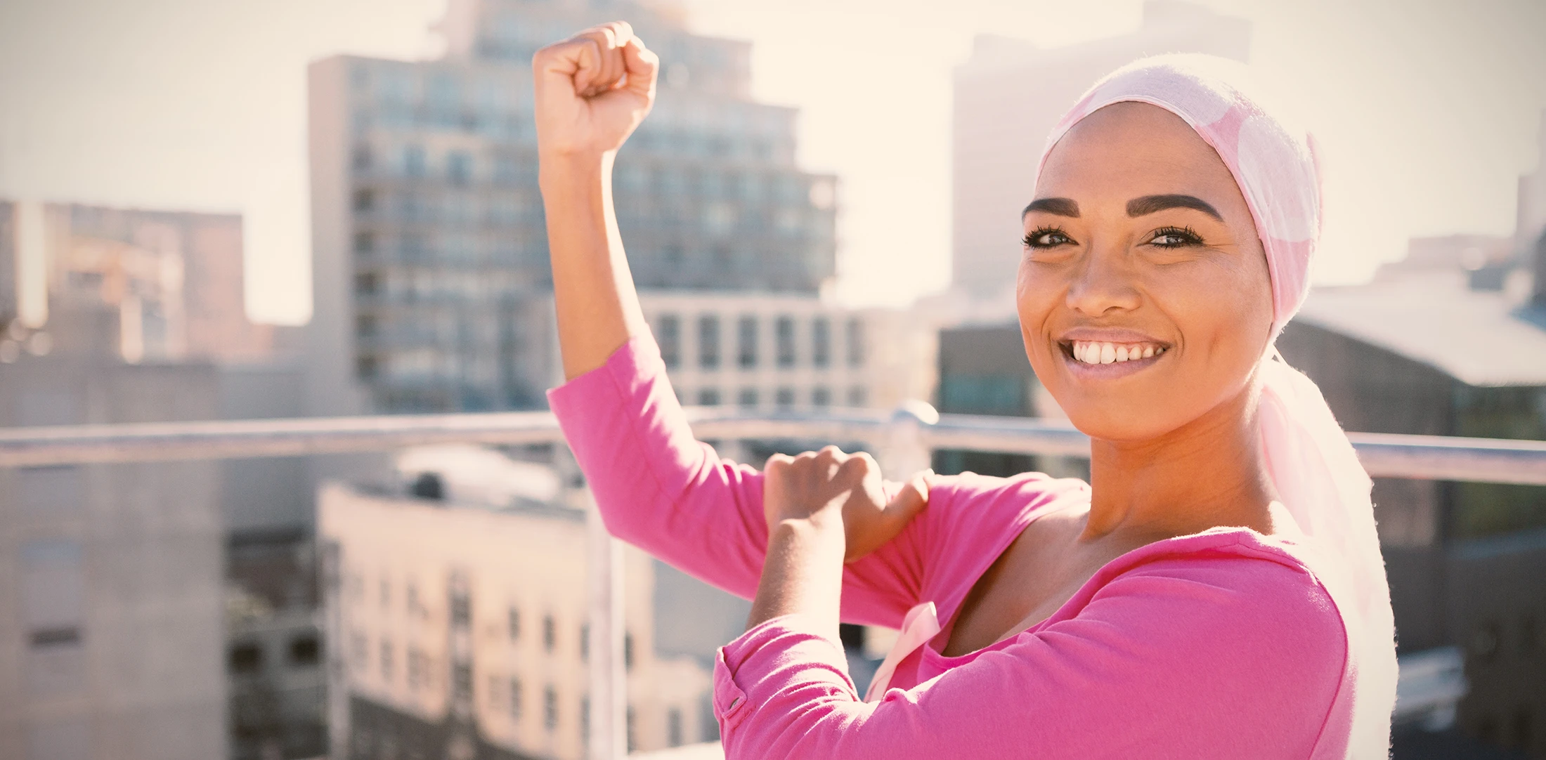 cancer surviving woman proudly showing off her biceps with a city in the background